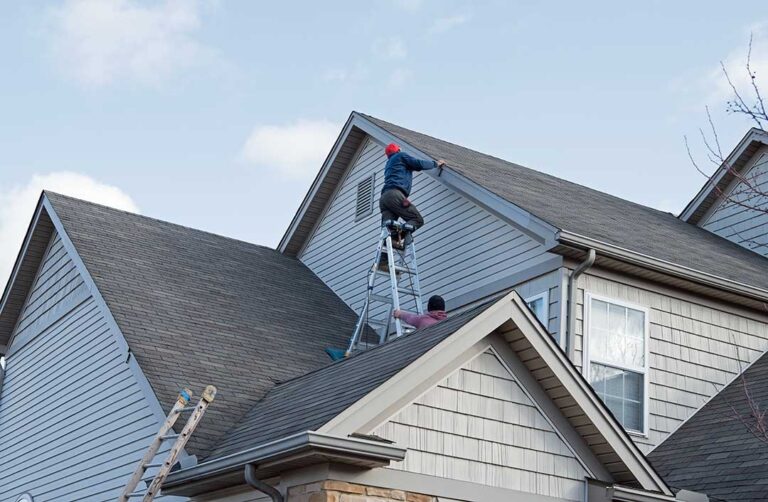 A local homeowner talking with a roofer while inspecting visible shingles and water damage on a residential roof.