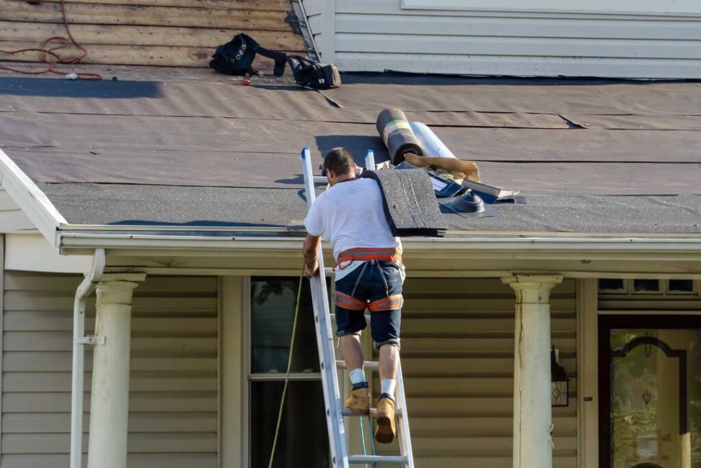 Homeowner checking roof gutters from the ground beside a seasonal residential house.