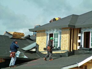 Roof workers examine reflective shingles, attic insulation, solar panels, and moisture sensors on a residential roof.