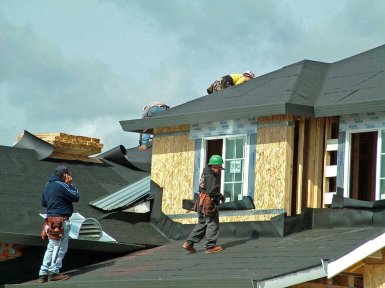 Roof workers examine reflective shingles, attic insulation, solar panels, and moisture sensors on a residential roof.